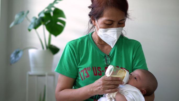 戴着防护口罩的亚洲妇女在家给婴儿喂奶