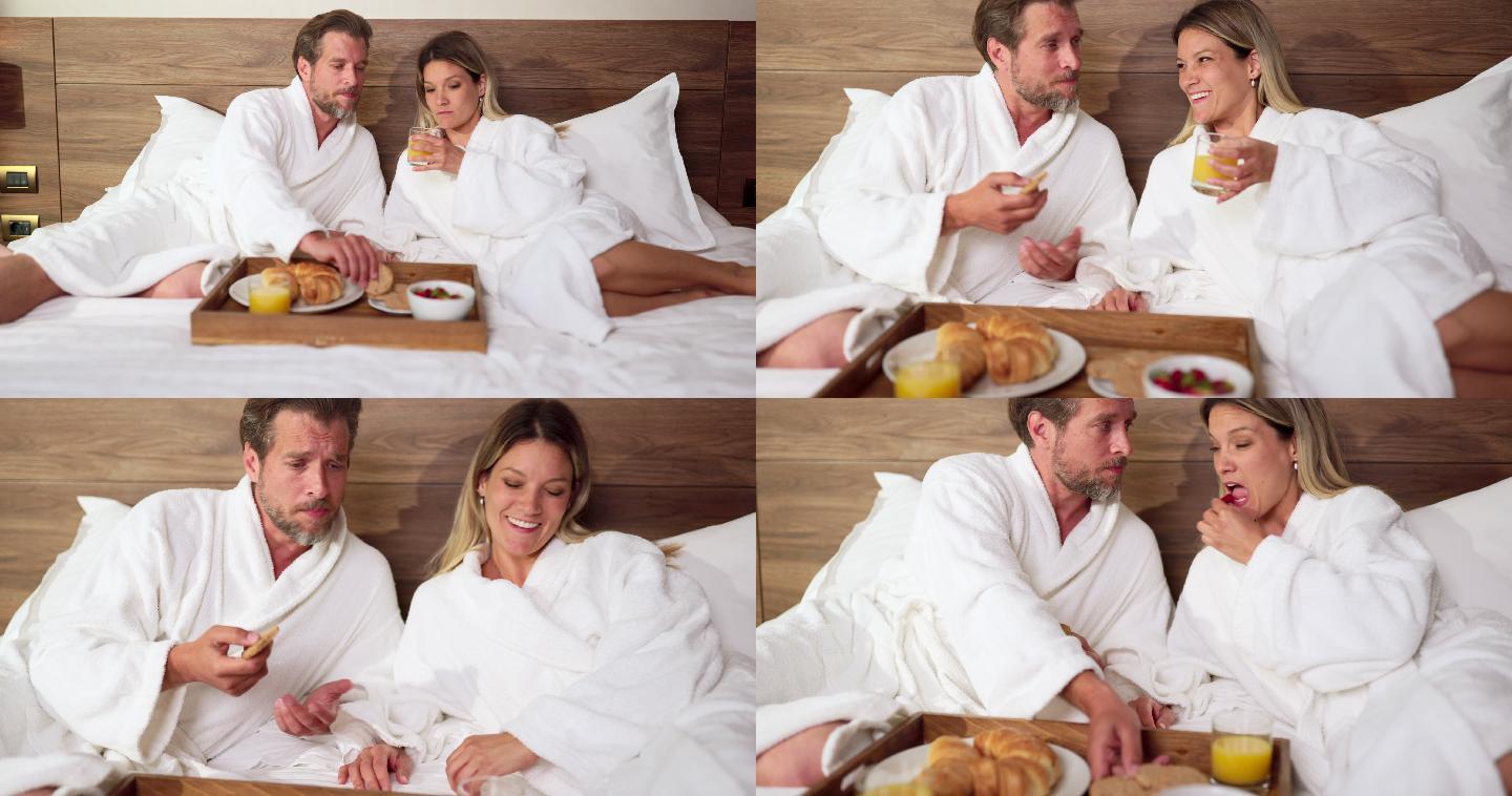 中年夫妇穿着浴袍在床上休息，吃早餐。