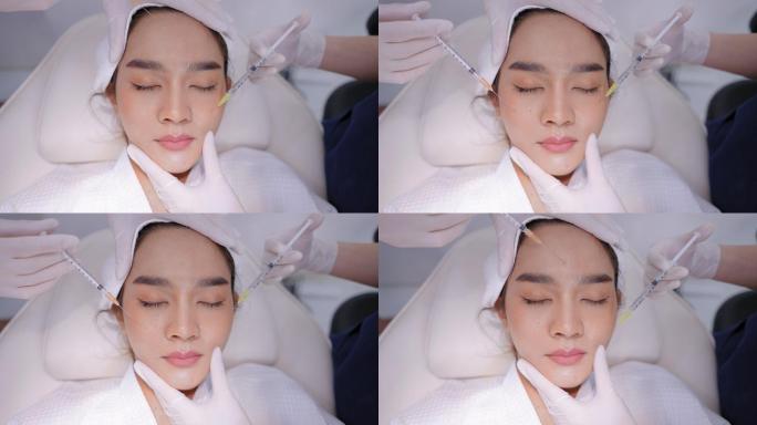 亚洲年轻漂亮的女性，穿着浴衣，头戴毛巾头巾，躺在医生面前，在额头皮肤和面部进行面部注射。亚洲年轻美丽