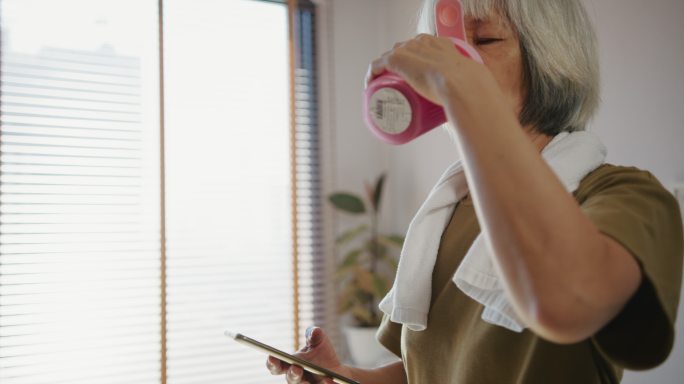 老年女性在锻炼和喝健康饮料后检查心率和卡路里燃烧状态