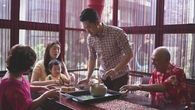 中国父亲在几代人的时间里端着中国茶，在下午茶聚期间在家里享用传统的中秋月饼和中国茶