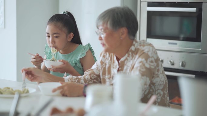 一位亚裔华裔老太太和她的孙女在厨房柜台前吃饺子