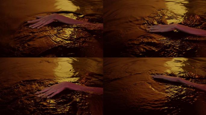 金色光滑的水面。女性的手轻轻地溅出并接触液体