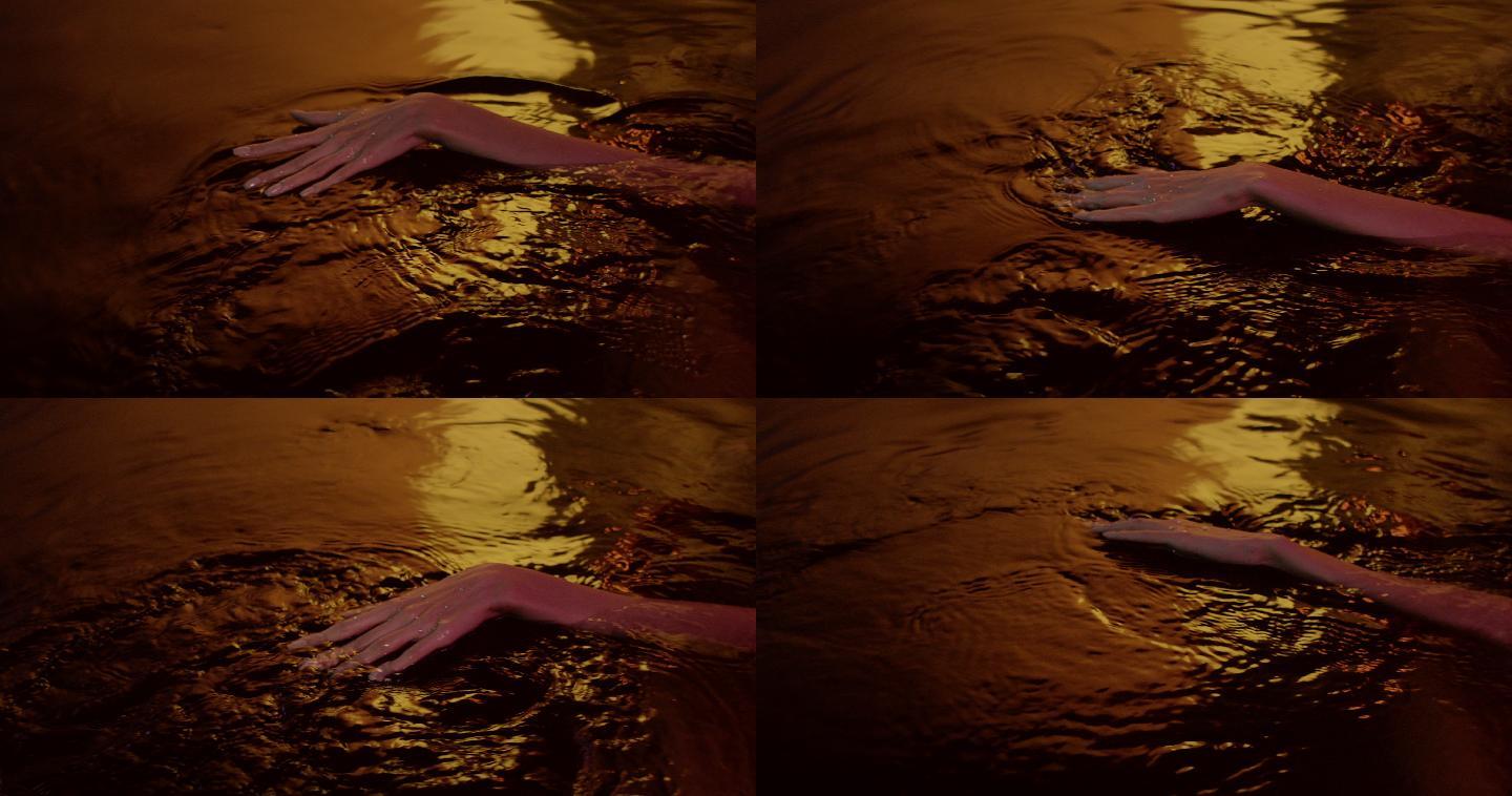 金色光滑的水面。女性的手轻轻地溅出并接触液体