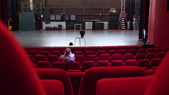 导演在一个空荡荡的剧院里写剧本，那里有红色的椅子和空荡荡的舞台