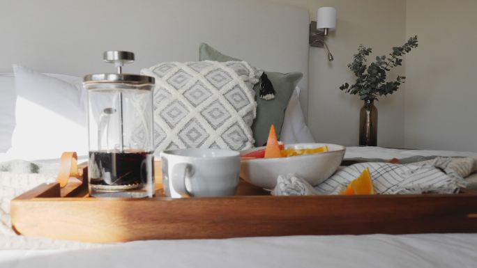 在阳光充足的床上，早餐托盘上放着法式咖啡和水果