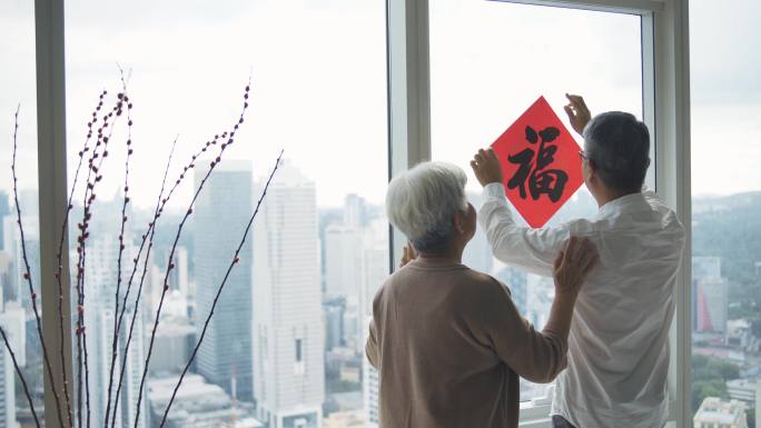 春节老人夫妇在窗户上用中国书法装饰客厅，为家庭团聚做准备