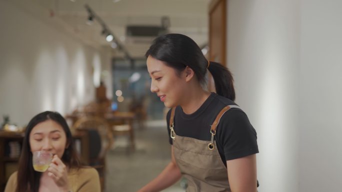 一位亚裔中国女服务员从厨房柜台接过托盘上的食物，为餐厅里的两位女性顾客提供服务