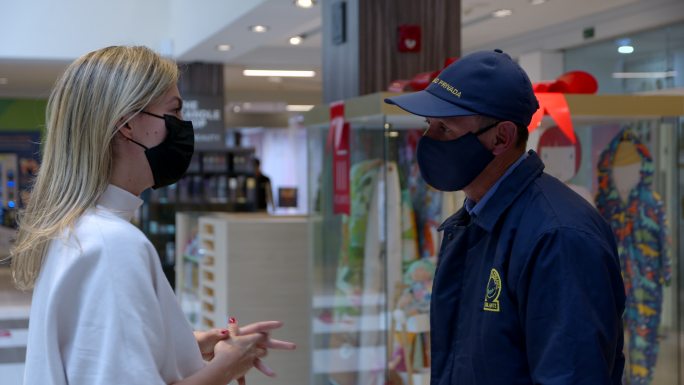 一名拉丁美洲女子在购物中心向保安问路，两人都戴着防护口罩
