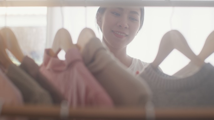 年轻的亚洲女性在家里客厅的衣橱里挑选时装。特写镜头。