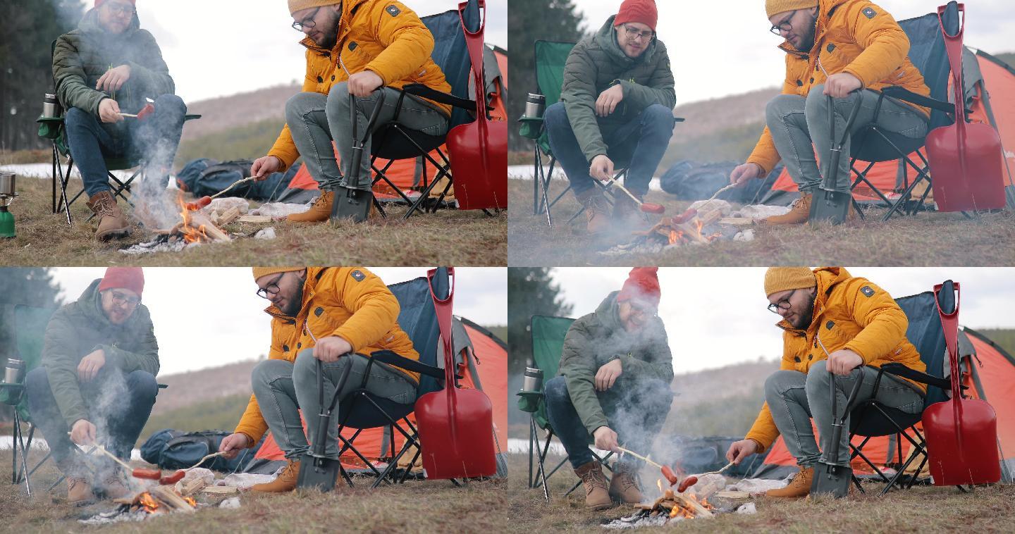 两个男人围坐在森林里的篝火旁烤香肠