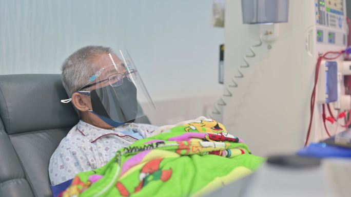 亚裔中国老人坐在椅子上，戴着面罩，在医院接受透析治疗
