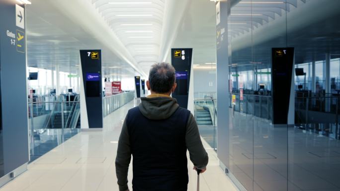 带着轮式旅行袋穿过机场航站楼的乘客