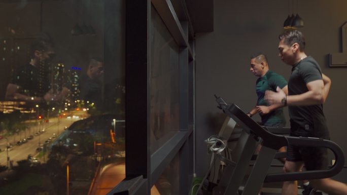 侧视图：大男子气概的男人们晚上在健身房一起跑步机，面对城市路灯