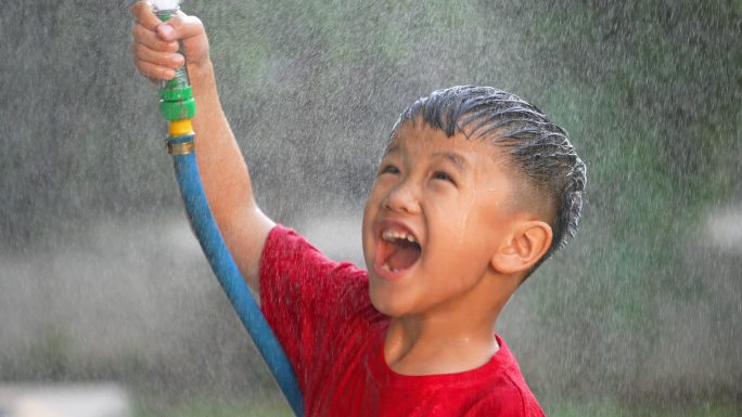 穿着靴子的亚洲小孩在公园里玩泼水和泥巴游戏。夏天和幸福的概念