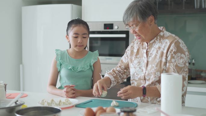 周末闲暇时间，亚裔中国小女孩在厨房向祖母学习做饺子
