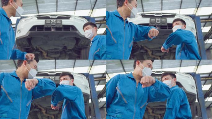 两名亚裔汽车修理工戴着口罩，用手肘碰触。在新冠疫情期间，车辆服务经理和盖伊工人团队在机械车库车间工作