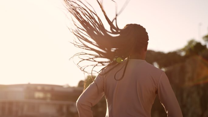 日落时分，一位留着长辫子头发的非洲裔美国女子在体育场跑步