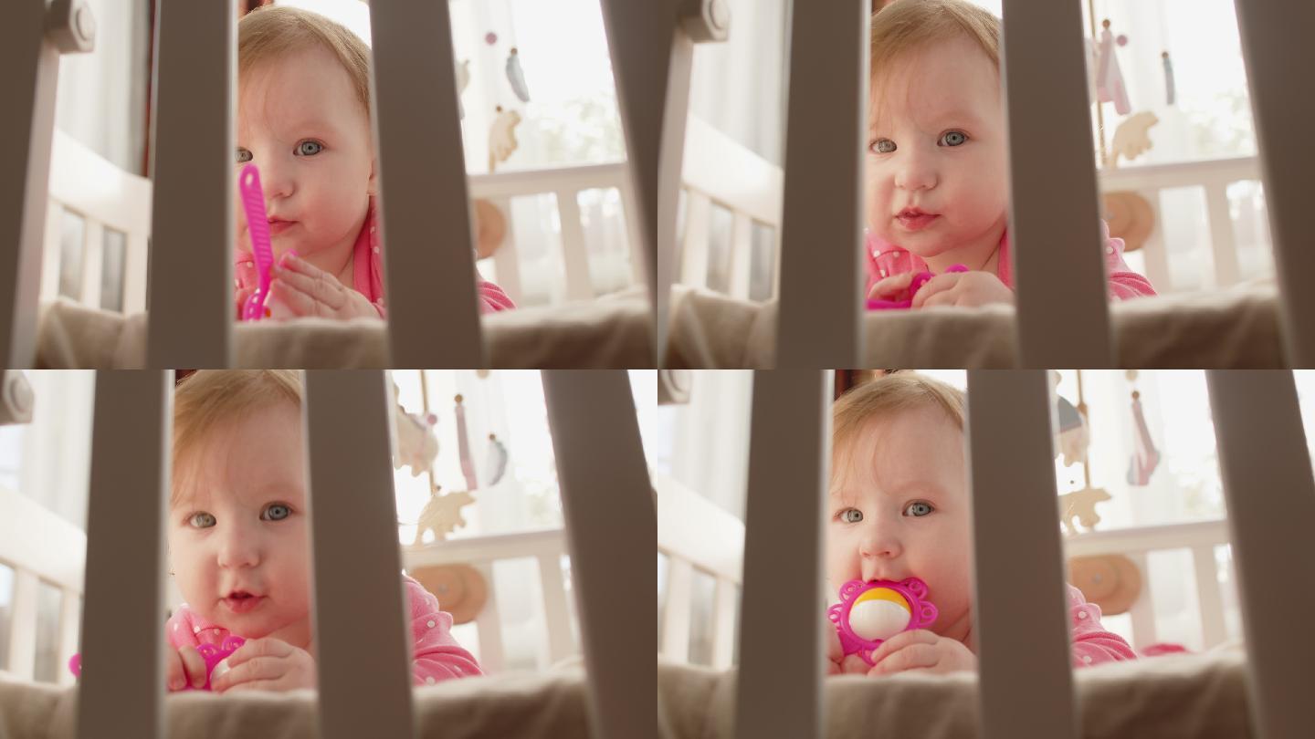 可爱快乐的女婴穿着粉色连体衣，戴着玩具拨浪鼓，在阳光明媚的早晨在室内玩得很开心