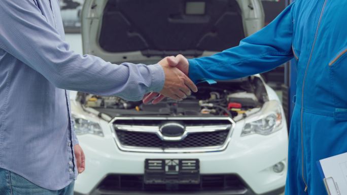 亚洲汽车修理工在车库与客户握手。在机械车间工作的车辆服务经理，在为客户检查和维护汽车发动机后感到高兴