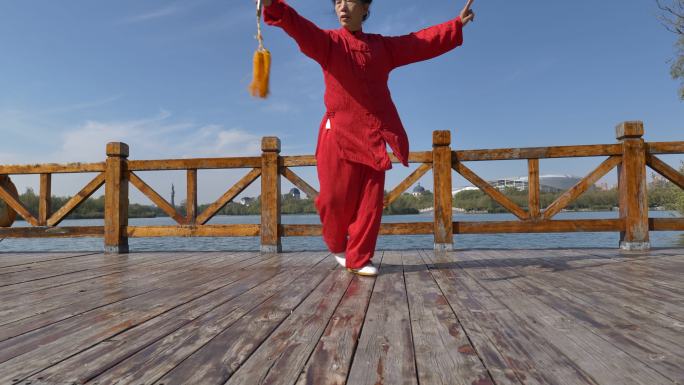 一位女士正在湖边练太极剑。