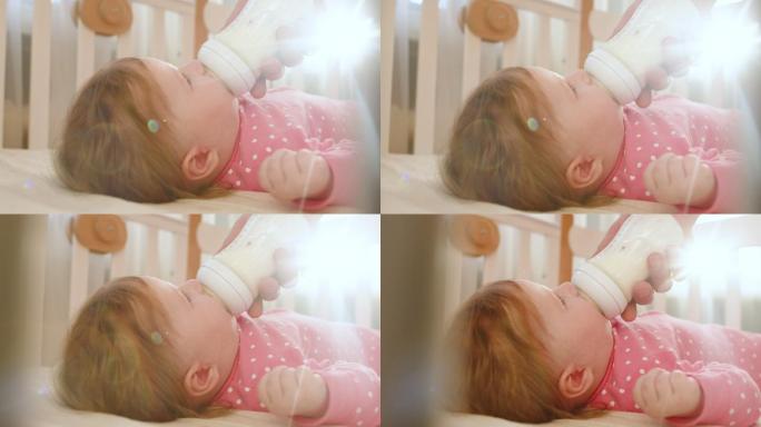 在一个阳光明媚的早晨，穿着粉色紧身衣的可爱快乐女婴在室内喝着婴儿奶瓶里的牛奶