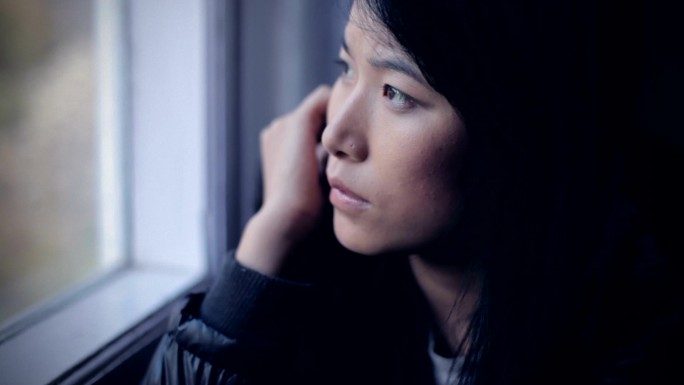 安静的亚洲女孩坐在窗边思考。