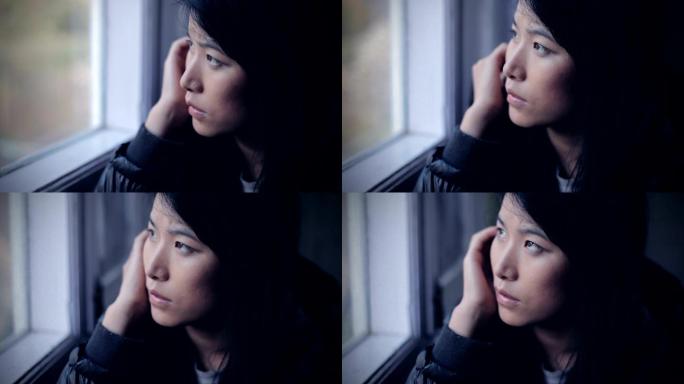 安静的亚洲女孩坐在窗边思考。