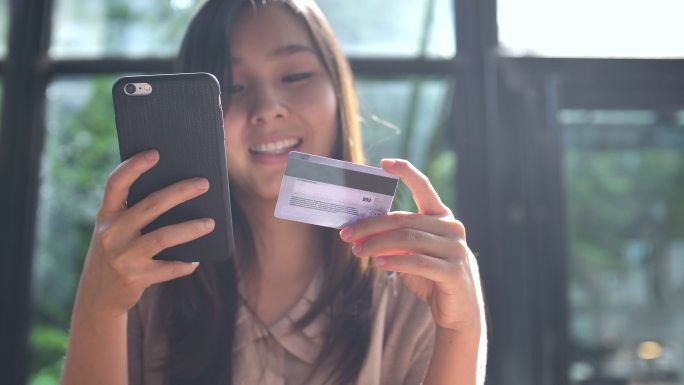 亚洲年轻女子用信用卡在手机上购物
