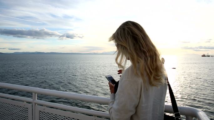 女人从船的甲板上眺望大海，拍下了照片