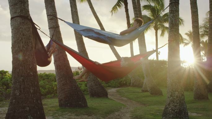 三个年轻人在棕榈树间的吊床上休息