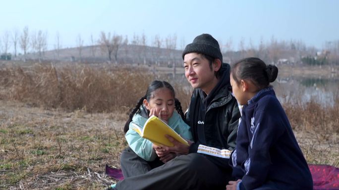 父亲坐在草地上陪女儿看书