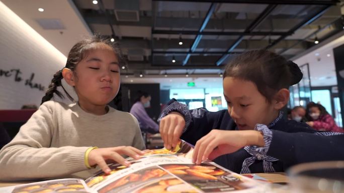 在餐厅翻阅菜单点餐的两个亚洲女孩