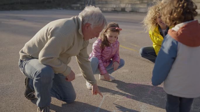 祖父带着女儿和孙女在混凝土上用粉笔画画