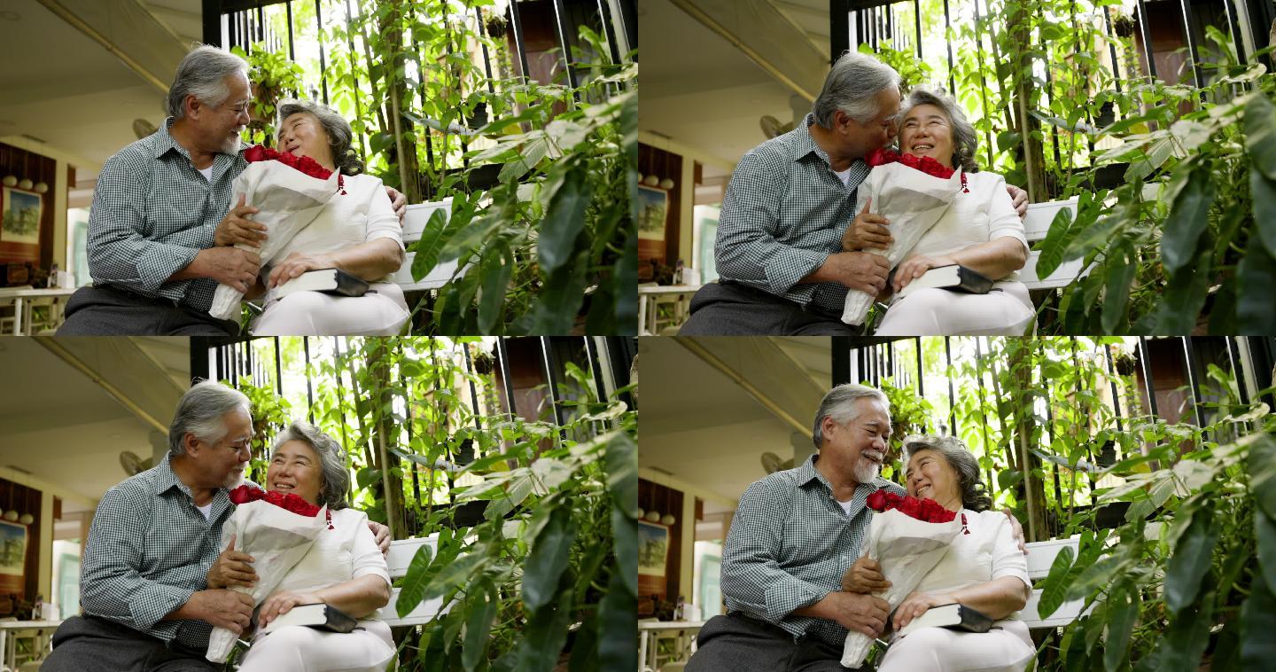 年迈的丈夫在家里用一束充满爱的玫瑰花给妻子惊喜。在结婚纪念日期间。老夫妇微笑着拥抱。