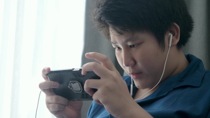 亚洲男孩在家里靠窗的沙发上玩手机游戏，这是一种生活方式。