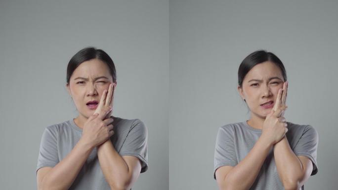 一名亚洲女子孤零零地站在灰色背景下，牙痛难忍。垂直视频4k分辨率。