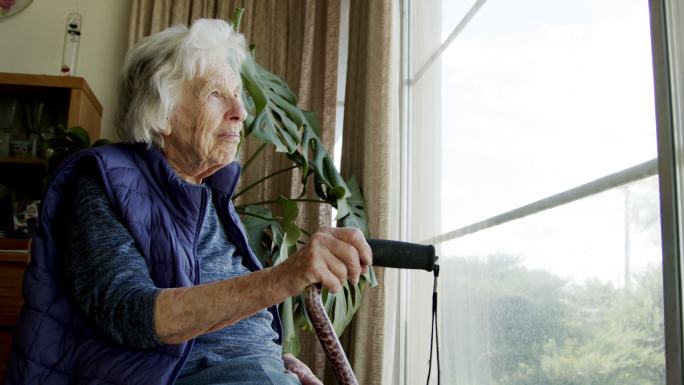 夏天，一位快乐、舒适的老年白人妇女在室内看着窗外的广角镜头