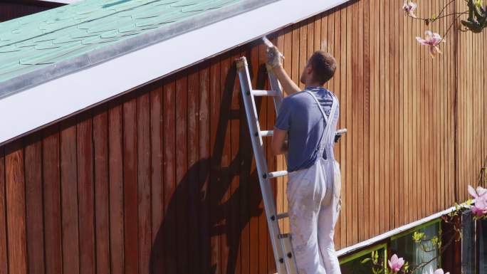 男油漆工对房屋外部的木镶板进行染色
