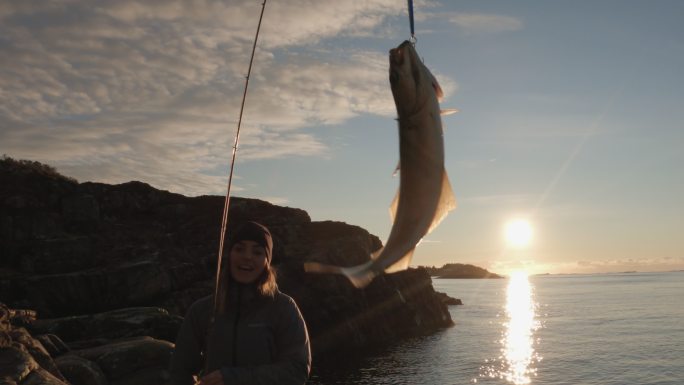挪威户外：女人在海里用鱼竿旋转钓鱼