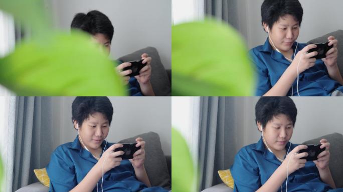 亚洲男孩在家里靠窗的沙发上玩手机游戏，这是一种生活方式。