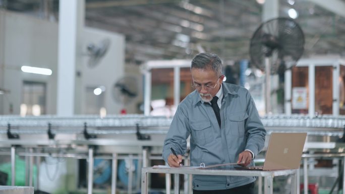 亚裔华裔高级工作人员在制造工厂计划生产计划中使用笔记本电脑