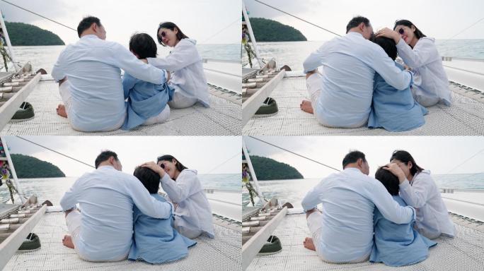 三口之家的后景：父亲、母亲和儿子坐在一艘漂浮在海上的豪华游艇上，在蹦床上相互拥抱，欣赏海景。在帆船上