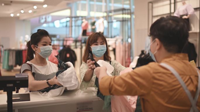 亚洲华人服装店的收银员在柜台上用口罩收到顾客的信用卡