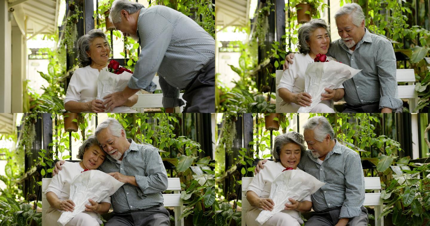 年迈的丈夫在家里用一束充满爱的玫瑰花给妻子带来惊喜。在结婚纪念日期间。老夫妇微笑着拥抱。