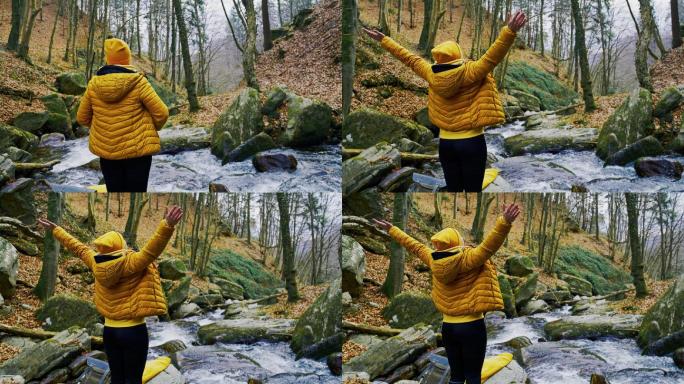 在森林里，一个女人伸出双臂站在流水旁的岩石上