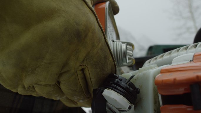 一个戴着手套的人在雪天在山上用电锯装满汽油