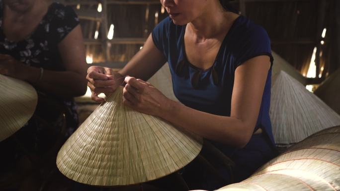 4k镜头的微光场景特写，越南工匠在越南坎托省阿披福村的传统老房子里制作传统越南帽子，传统艺术家概念