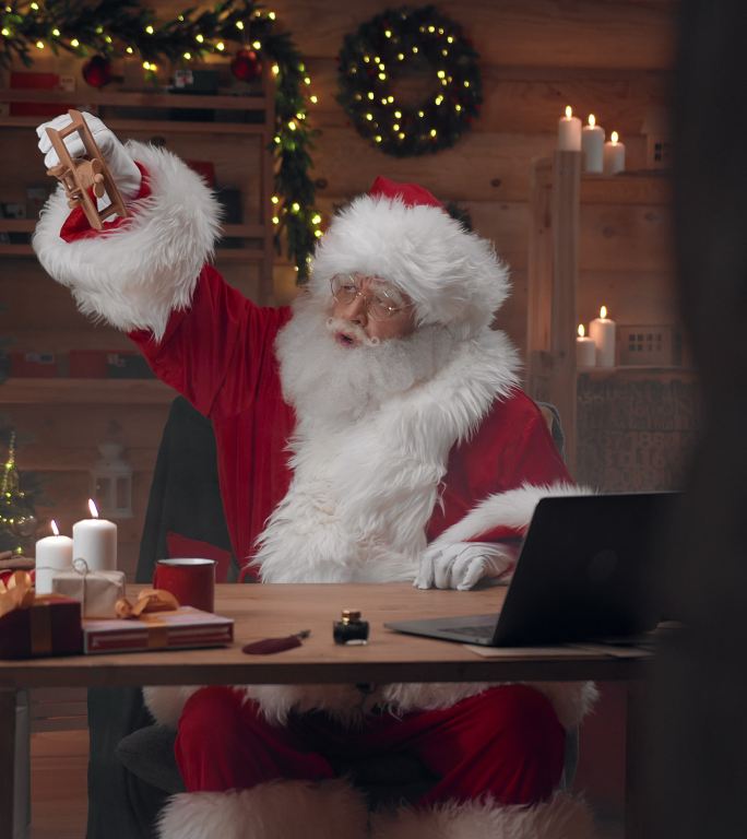 圣诞老人展示了坐在办公室桌子旁玩一架可爱的木制飞机是多么有趣