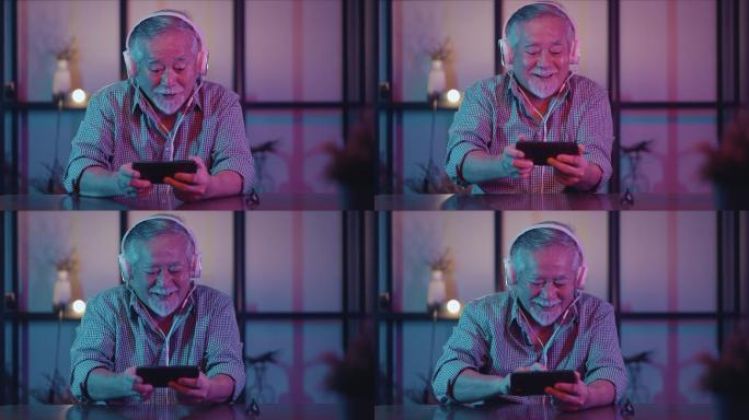 亚洲退休老年男性喜欢玩游戏和比赛智能手机在线沙发客厅家居室内背景，亚洲老年男性在家里使用智能手机玩游